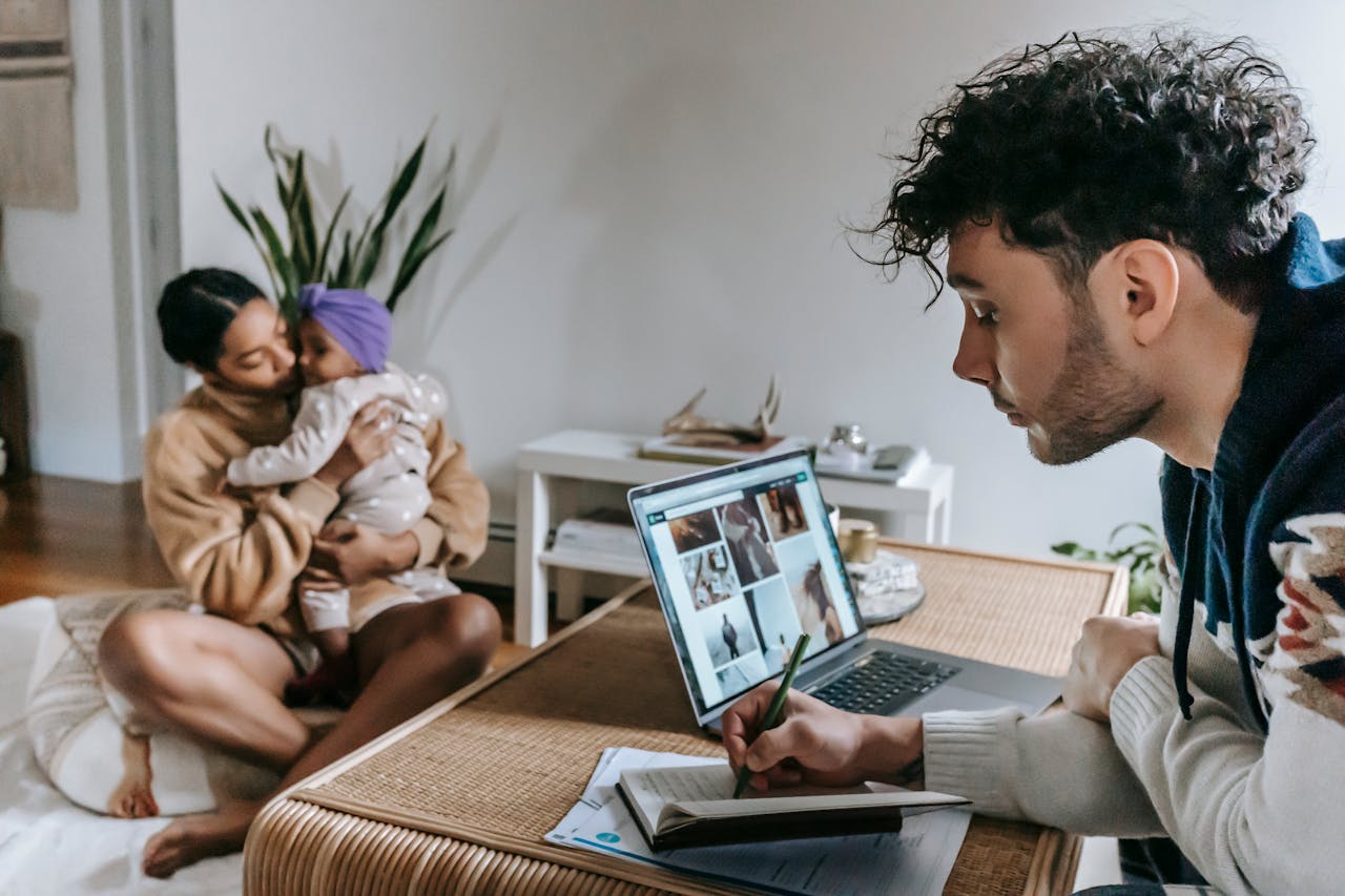 A dad at his laptop, and a mum holding their child, at home