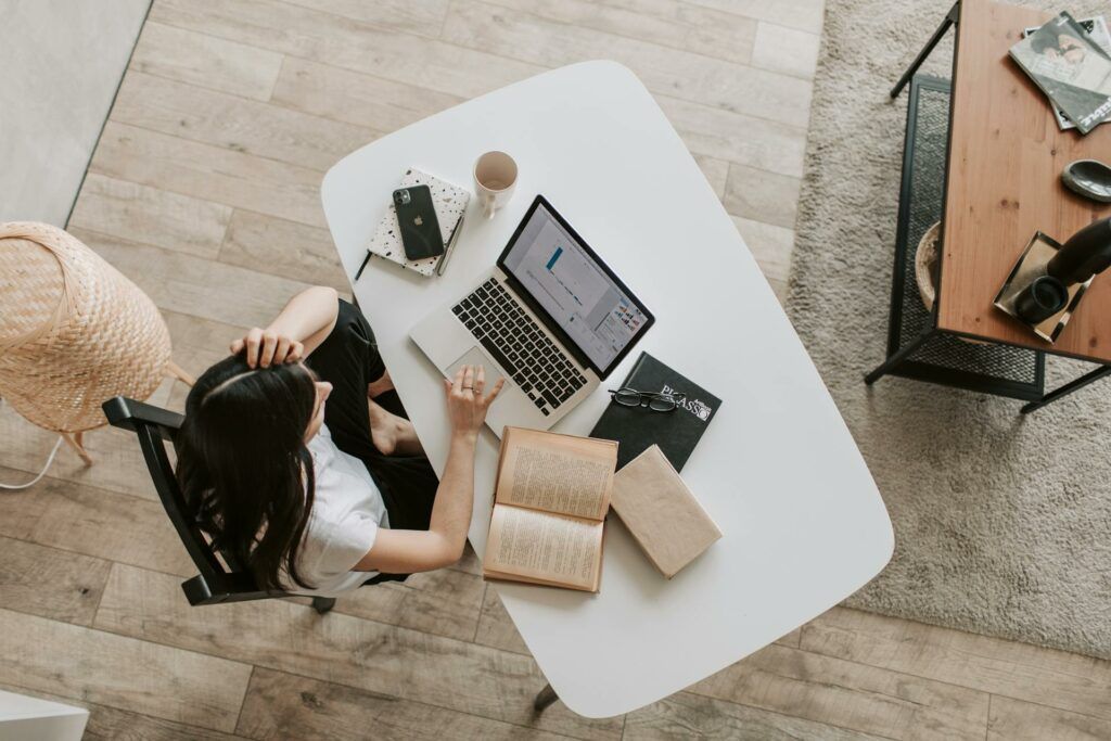 A lady at a desk, working from home. There is a laptop and book on the desk.