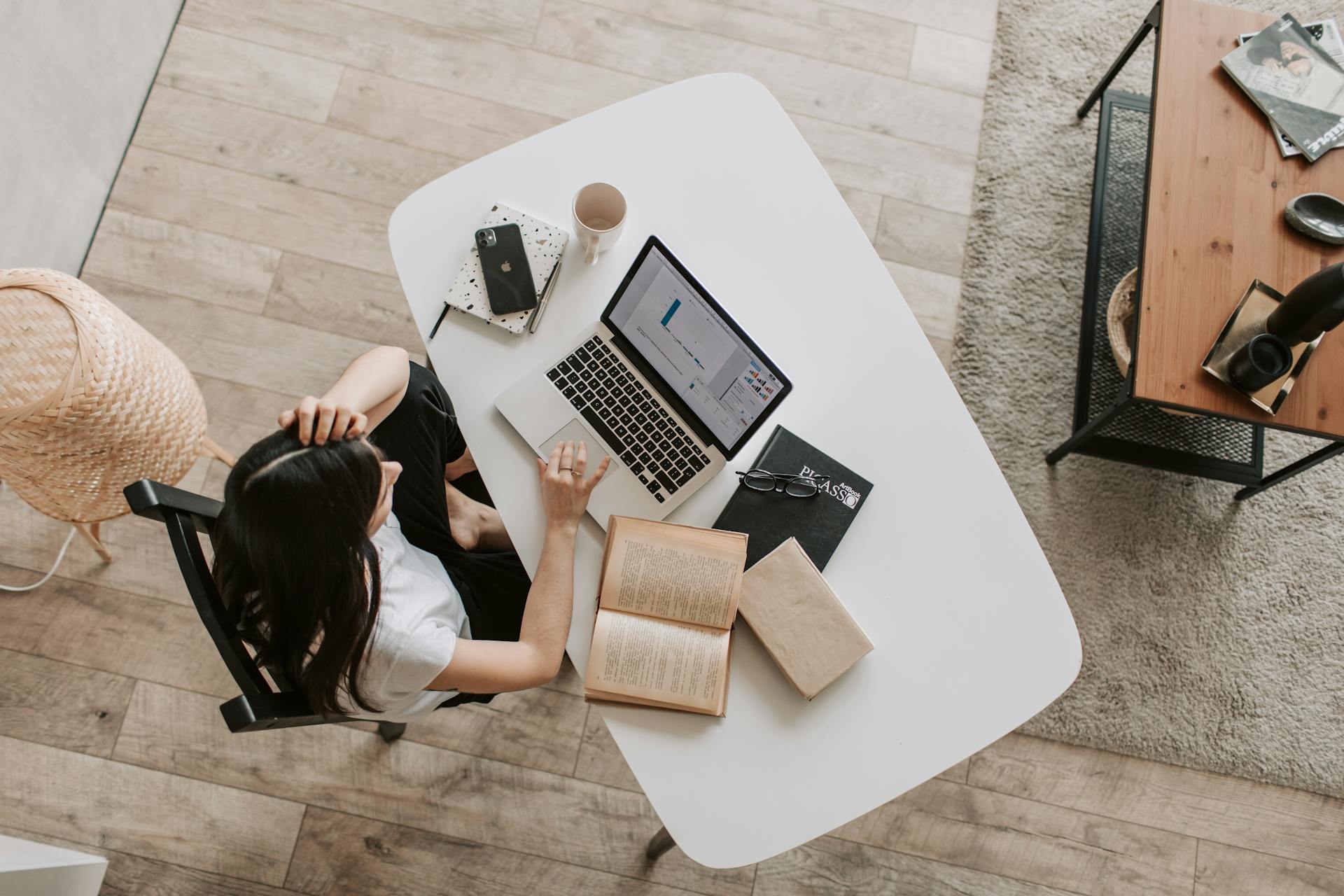 A lady at a desk, working from home. There is a laptop and book on the desk.