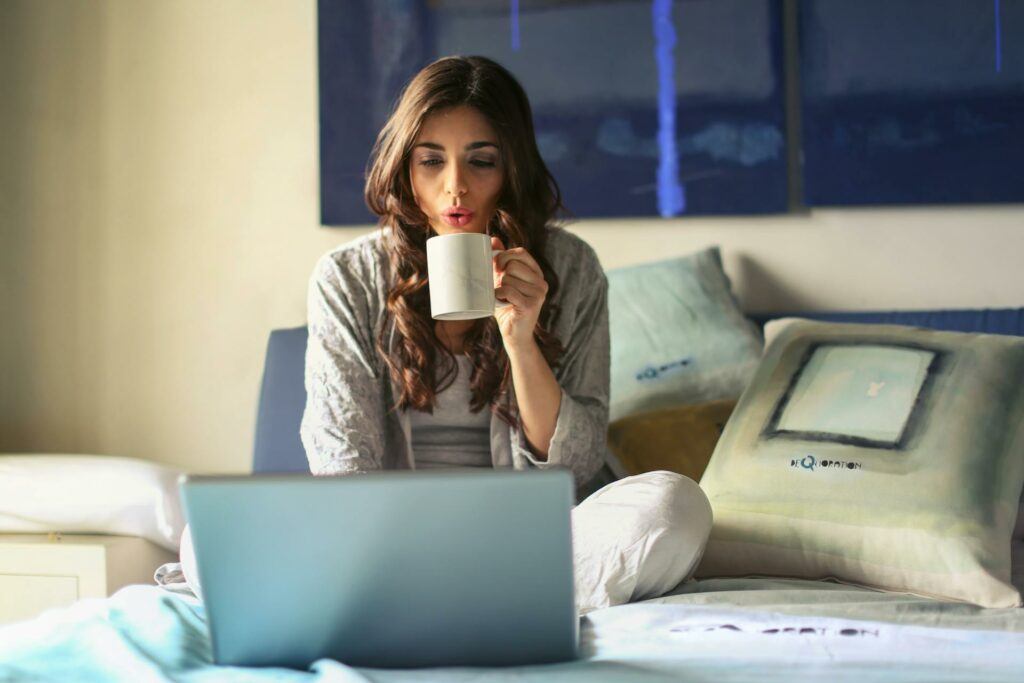 A lady sitting cross-legged on the floor, in front of a laptop, with a coffee