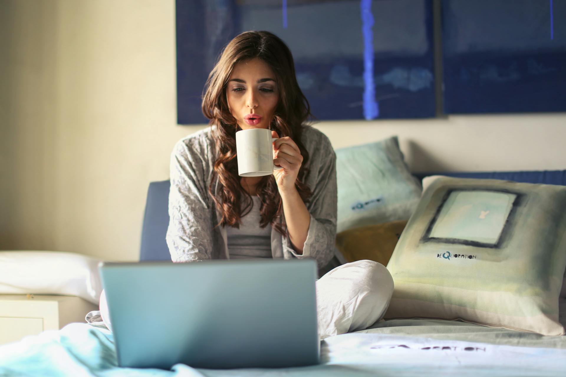 A lady sitting cross-legged on the floor, in front of a laptop, with a coffee