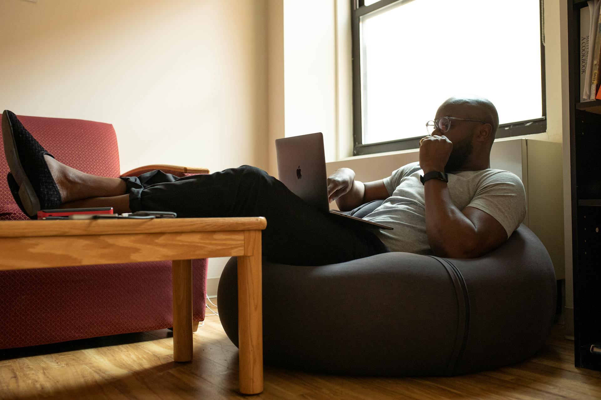 A man sitting comfortably in a beanbag, at home, with a laptop
